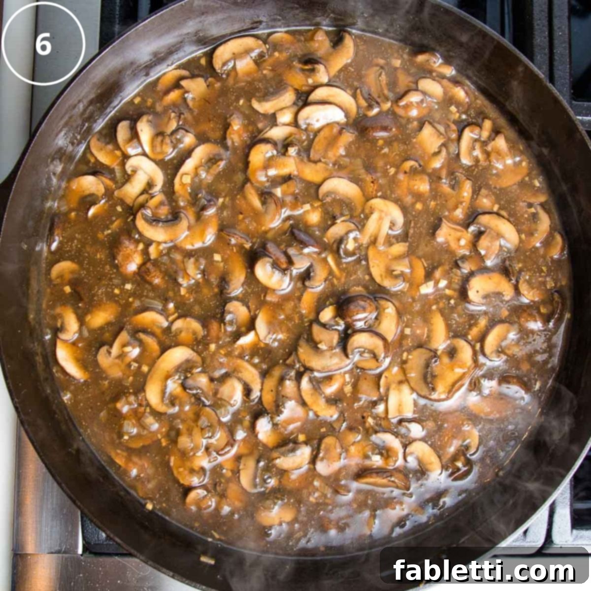 Hearty Vegan Mushroom Stroganoff 10 Sliced mushrooms simmering in a glossy brown sauce within a cast iron skillet after deglazing.