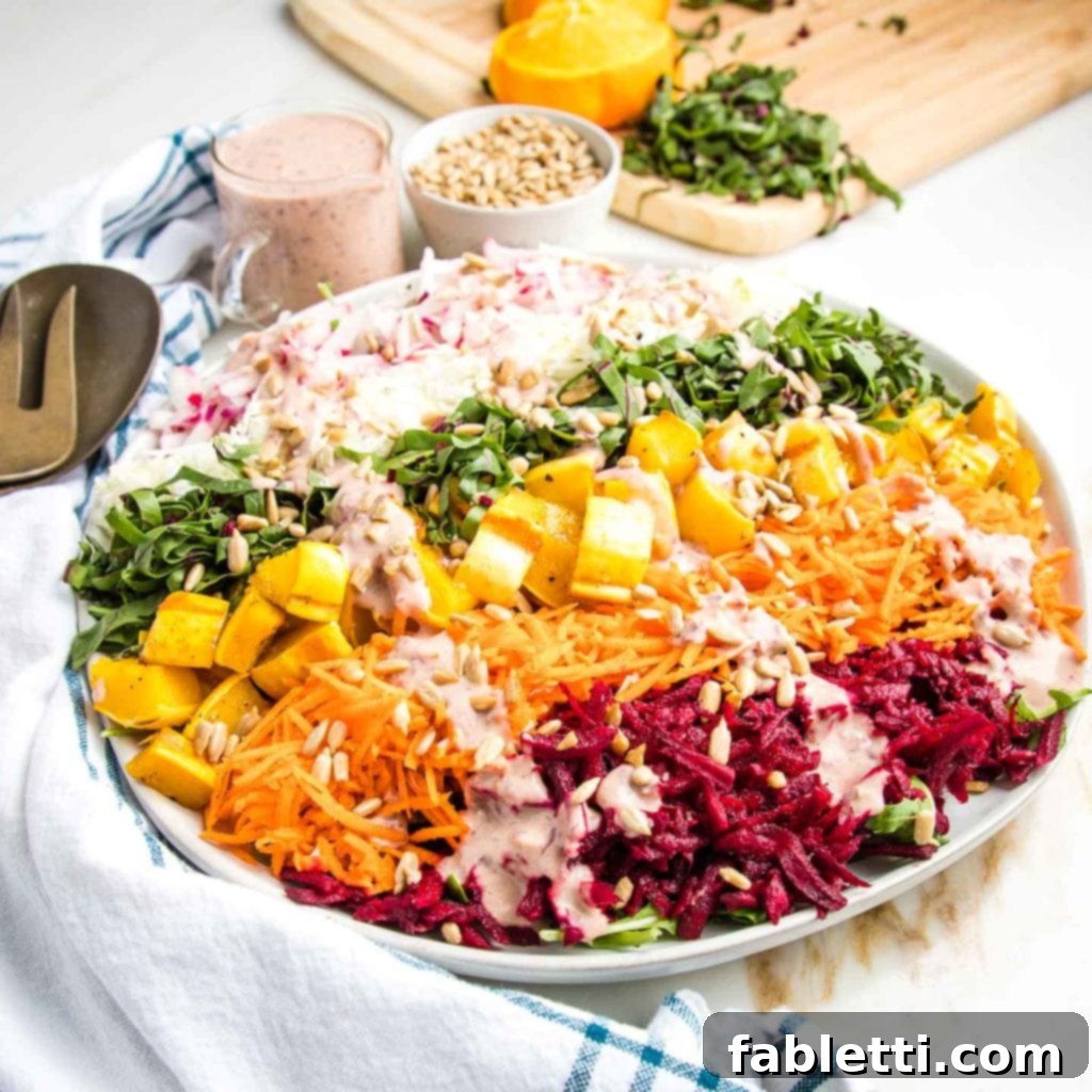 A close-up shot of the finished Shredded Rainbow Salad, artfully arranged on a large white platter. The vibrant, shredded vegetables form distinct colorful stripes, beautifully drizzled with the creamy pink, oil-free dressing. The textures are visibly crisp and fresh, inviting a delicious and healthy meal.