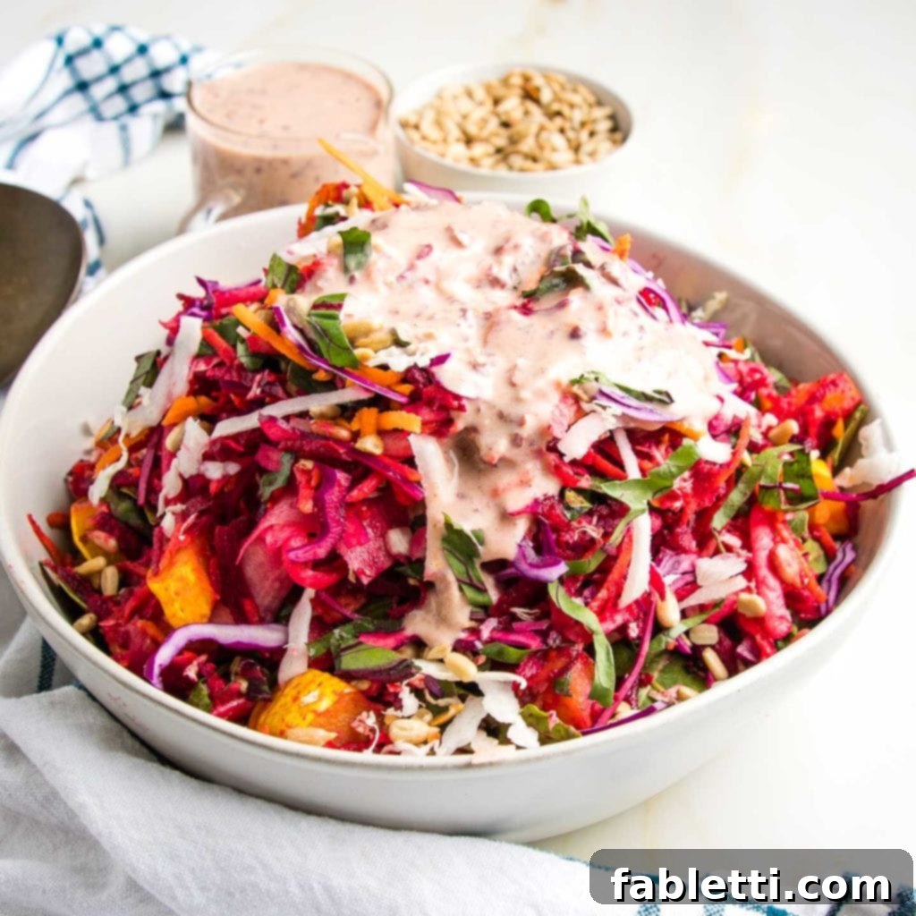 A vibrant, colorful Shredded Rainbow Salad, gently tossed and artfully arranged on a white plate, showcasing the various shredded vegetables. A generous drizzle of creamy pink dressing adorns the top, highlighting the fresh and inviting appeal of the dish.