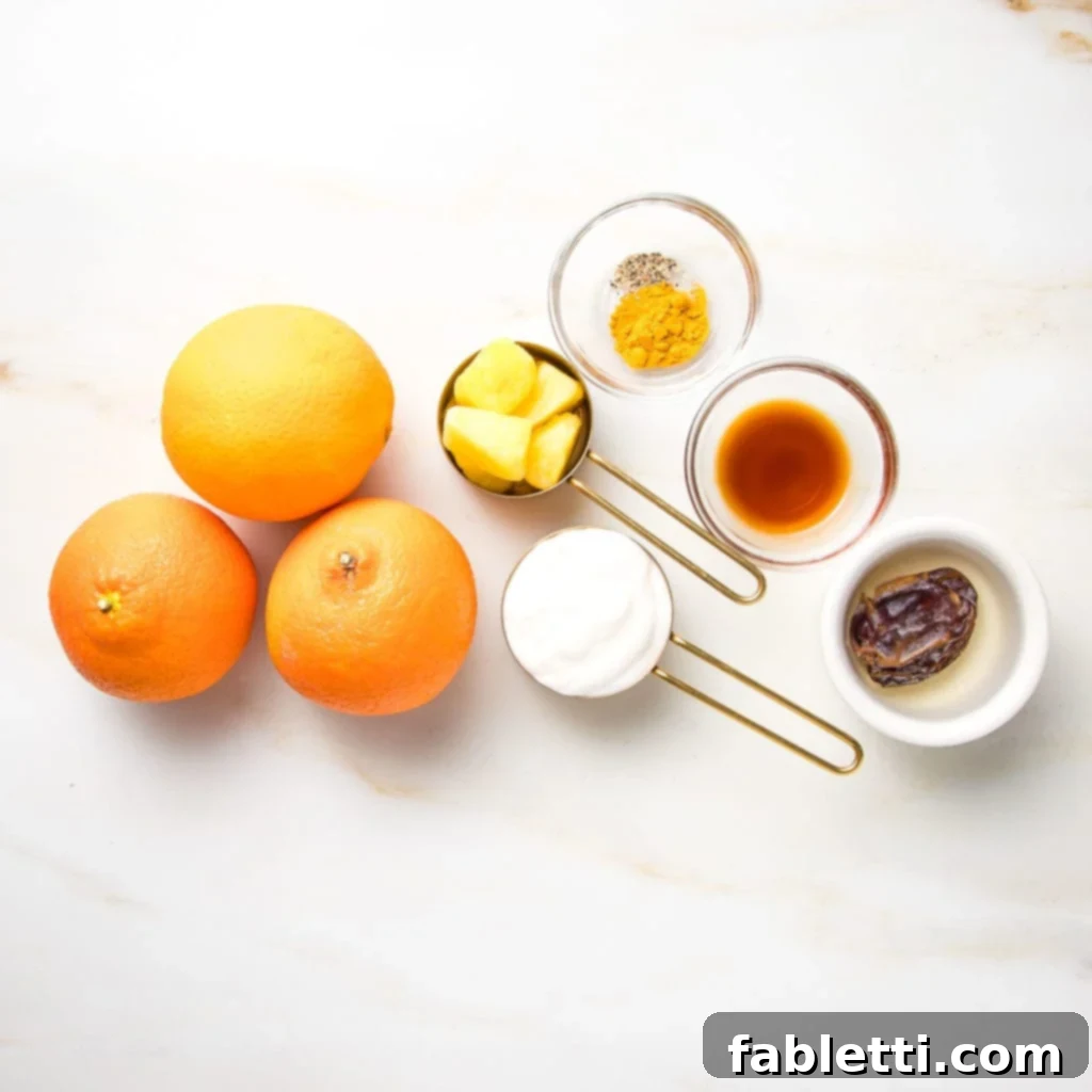 Frothy Orange Julius Delight 4 A flat lay showing the ingredients for an orange julius smoothie: fresh oranges, frozen pineapple chunks, a container of plant-based yogurt, a small bowl of turmeric and black pepper, a vanilla extract bottle, and a medjool date.