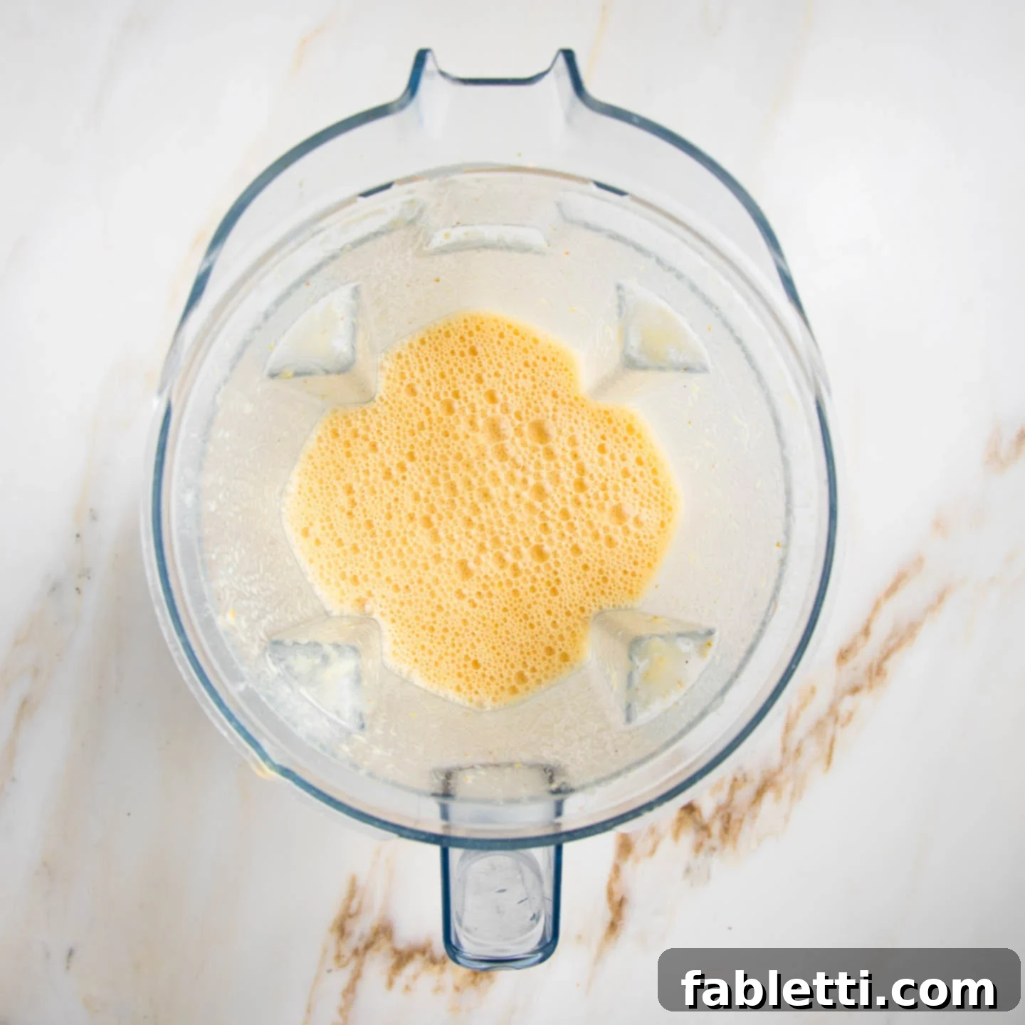 Frothy Orange Julius Delight 7 A close-up shot of frothy orange smoothie in a blender pitcher after blending, showing its smooth, creamy texture.