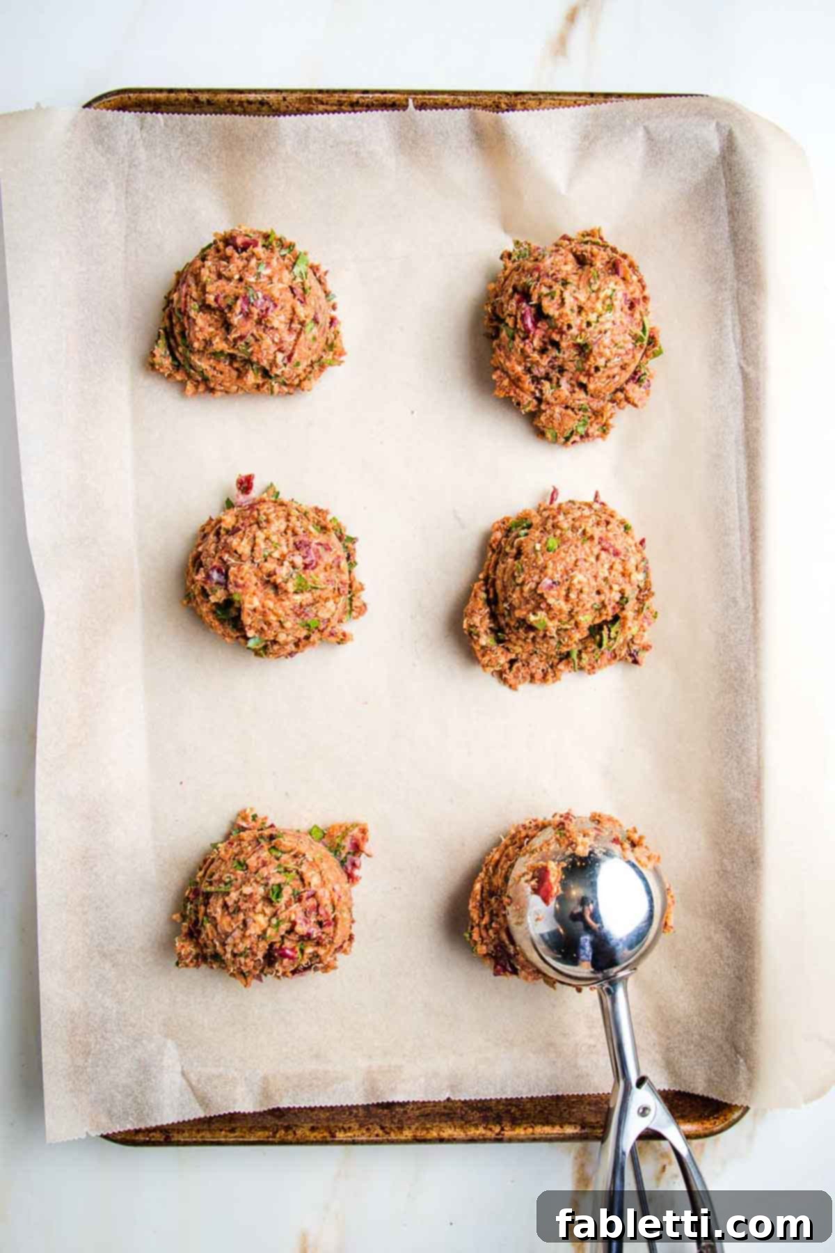 A large scooper portioning out uniform mounds of the veggie burger mixture onto a baking sheet lined with parchment paper, preparing for patty formation.
