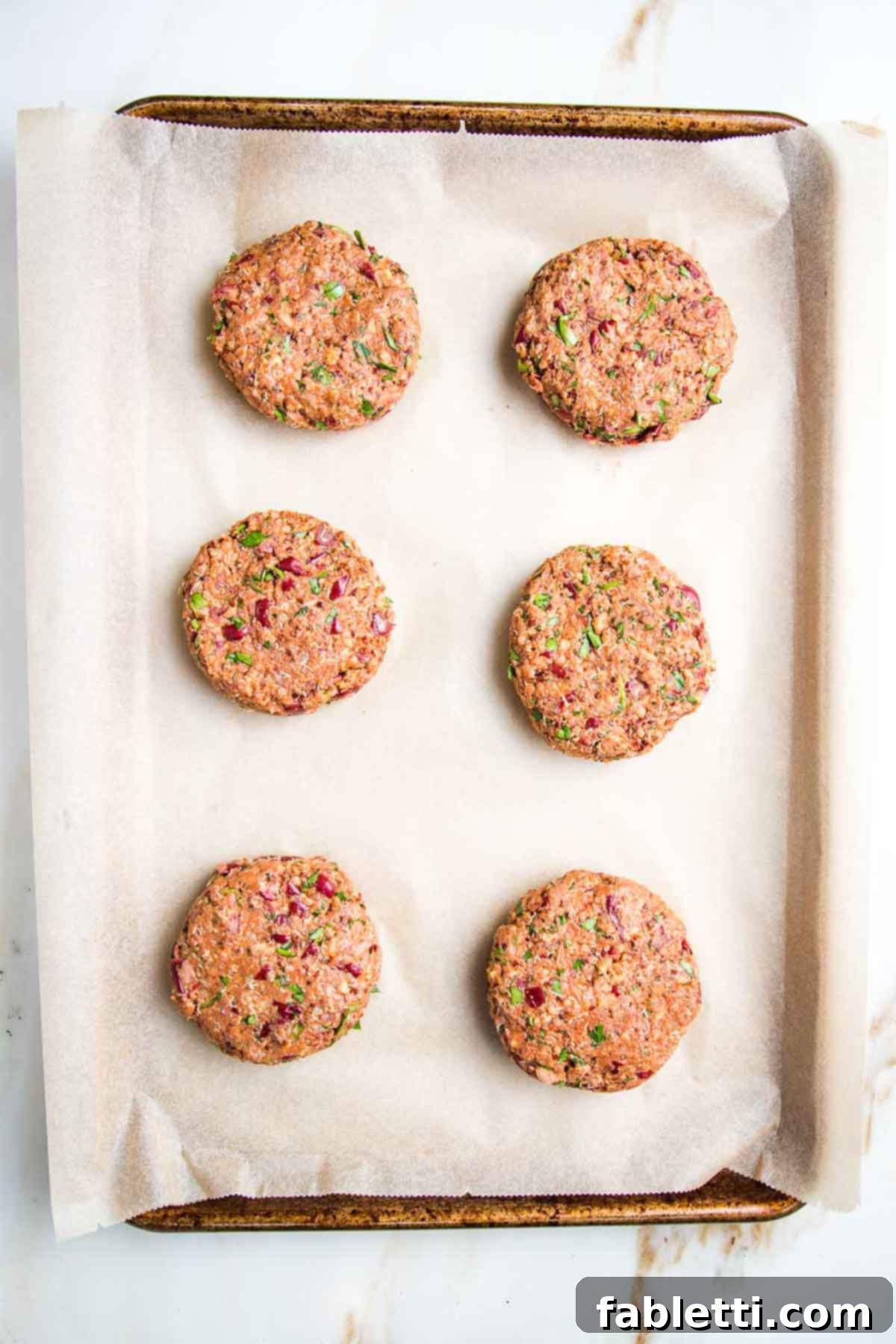 Six perfectly formed, uniformly thick veggie burger patties arranged neatly on a parchment-lined baking sheet, ready for baking.