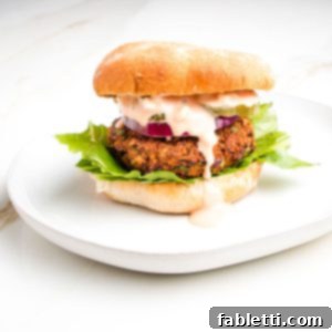 A hearty quinoa veggie burger in a bun, adorned with crisp lettuce and a luscious sauce gently dripping down the side, inviting you to take a bite.