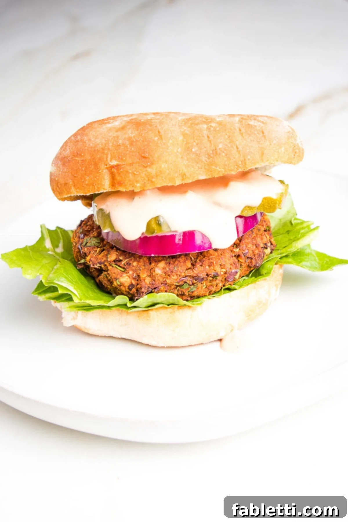 A perfectly assembled quinoa veggie burger in a bun, topped with crisp lettuce, a juicy tomato slice, and a generous dollop of creamy secret sauce, ready to be devoured.