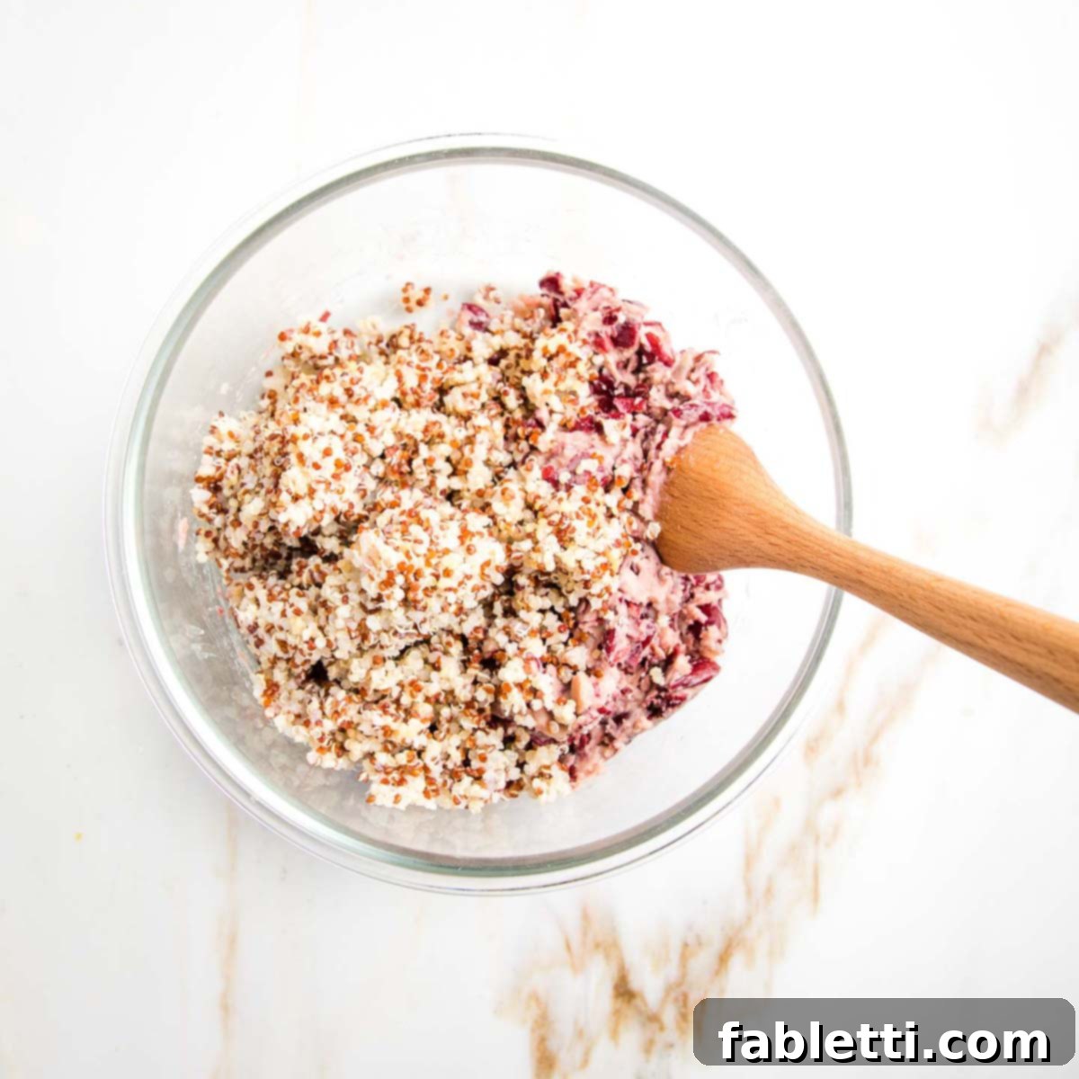 A mixture of fluffy cooked quinoa and creamy mashed kidney beans in a glass bowl, with a wooden spoon resting inside, ready for the next ingredients.