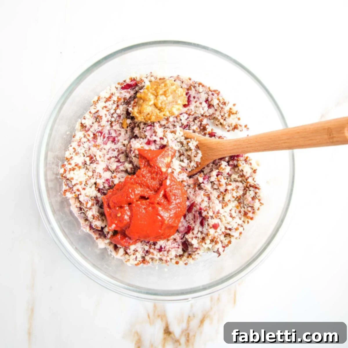 Rich tomato paste and savory miso paste dolloped directly on top of the mixed quinoa and mashed bean base in a glass bowl, ready to be incorporated.