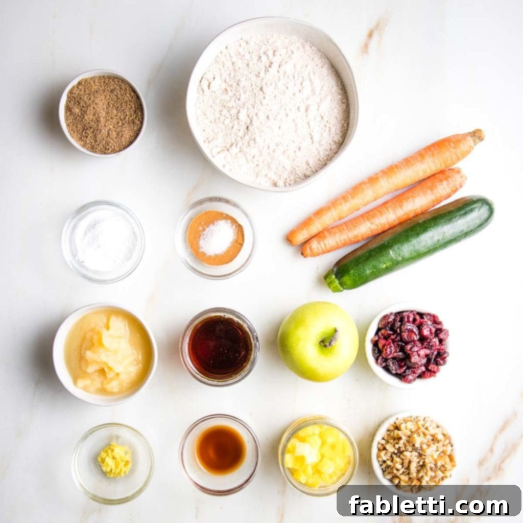 A selection of fresh ingredients for Morning Glory Muffins, including carrots, zucchini, apples, dried cranberries, walnuts, and bottles of maple syrup and vanilla extract, arranged on a rustic wooden surface.