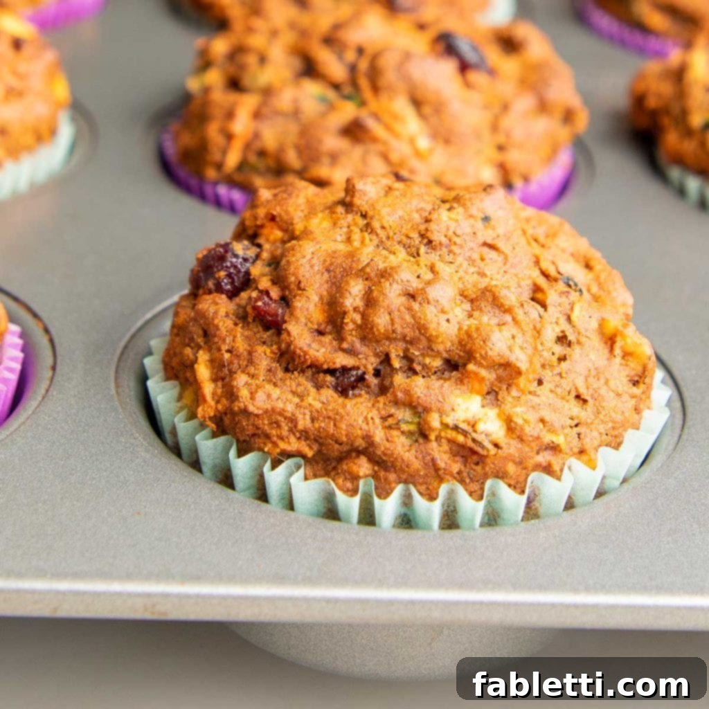 A close-up view of a perfectly baked Morning Glory Muffin, still in its pan, showcasing a beautiful rise, golden-brown crust, and a light blue paper liner.