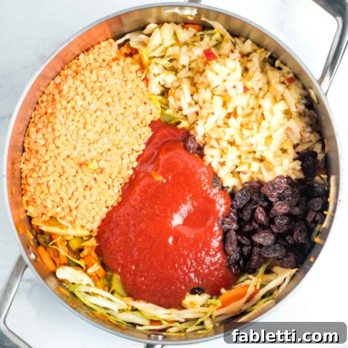 Tangy Vegan Cabbage Soup 8 Adding red lentils, tomato sauce, shredded apple, and raisins to the pot.