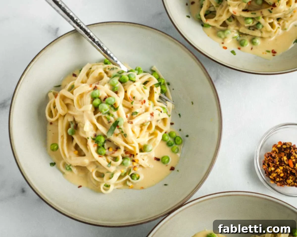 Bowl of Fettuccine Alfredo with peas and crushed red pepper flakes.