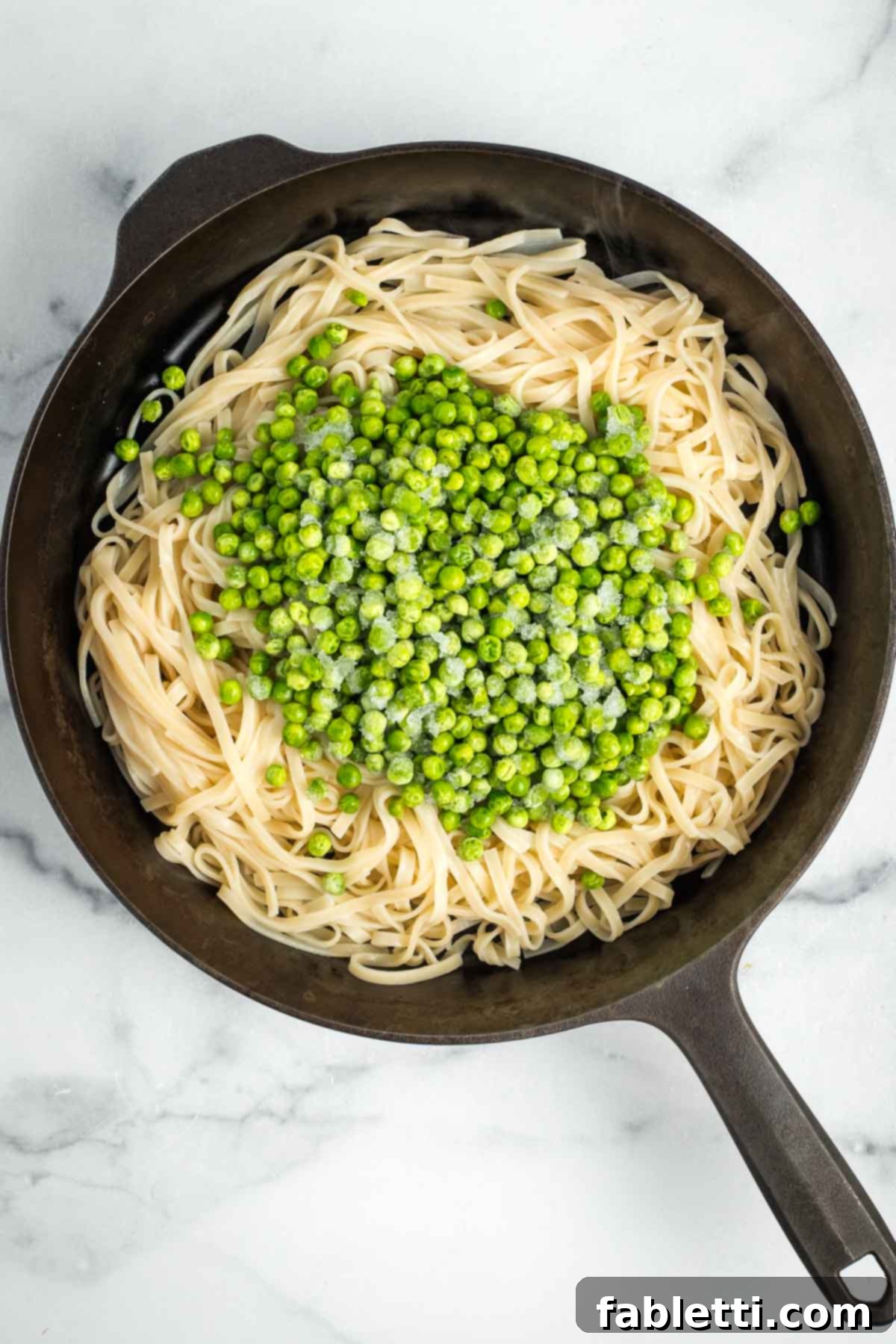 Cast iron skillet with cooked noodles and frozen peas.