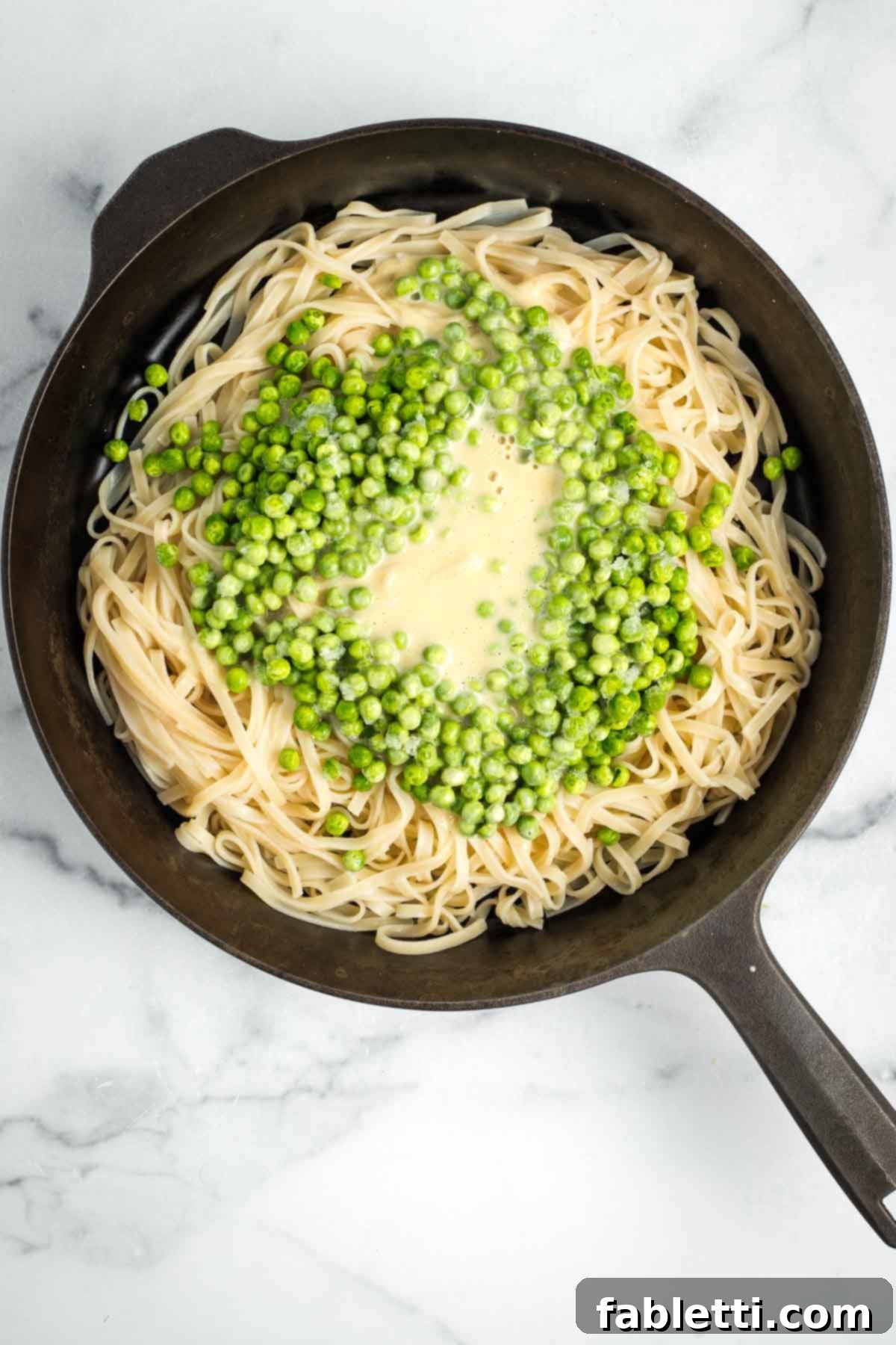 Cast iron skillet filled with noodles, peas, and creamy Alfredo sauce.
