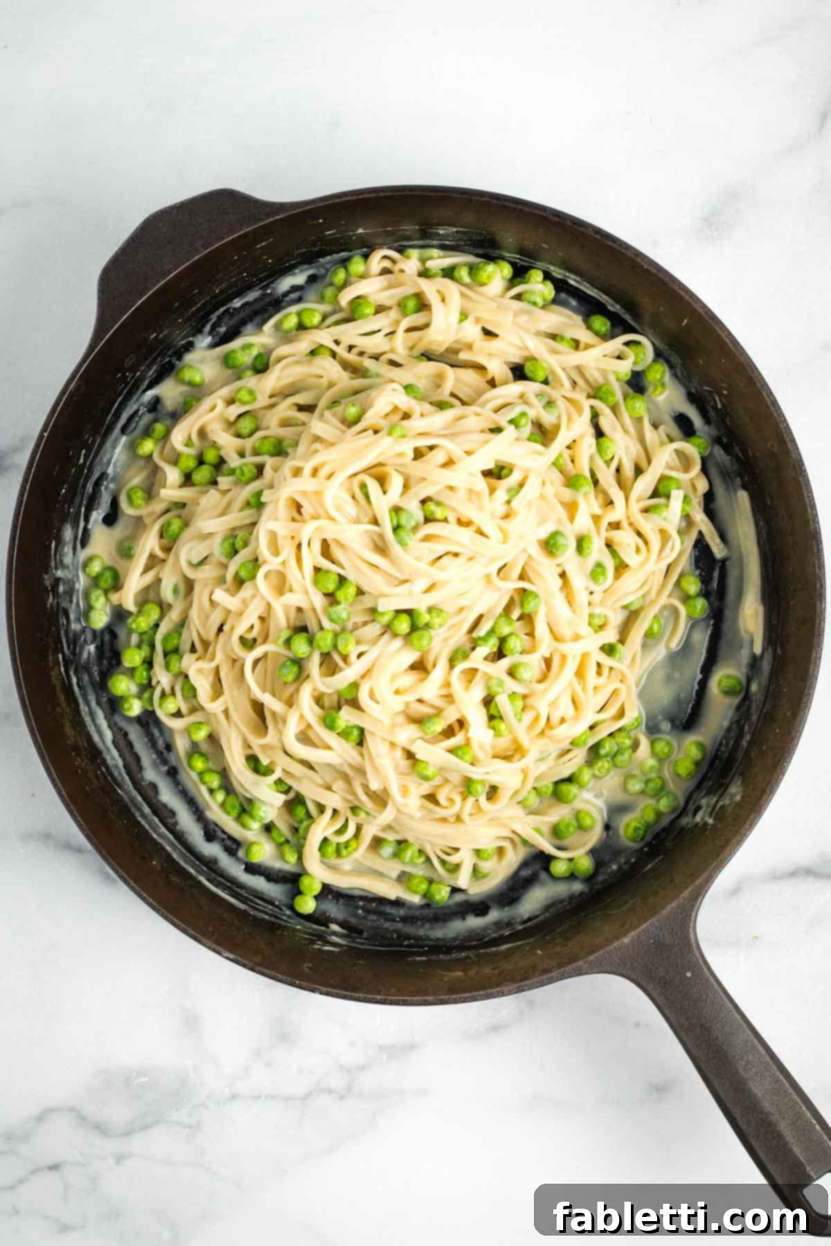 Creamy Vegan Fettuccine Alfredo with peas in a cast iron skillet.