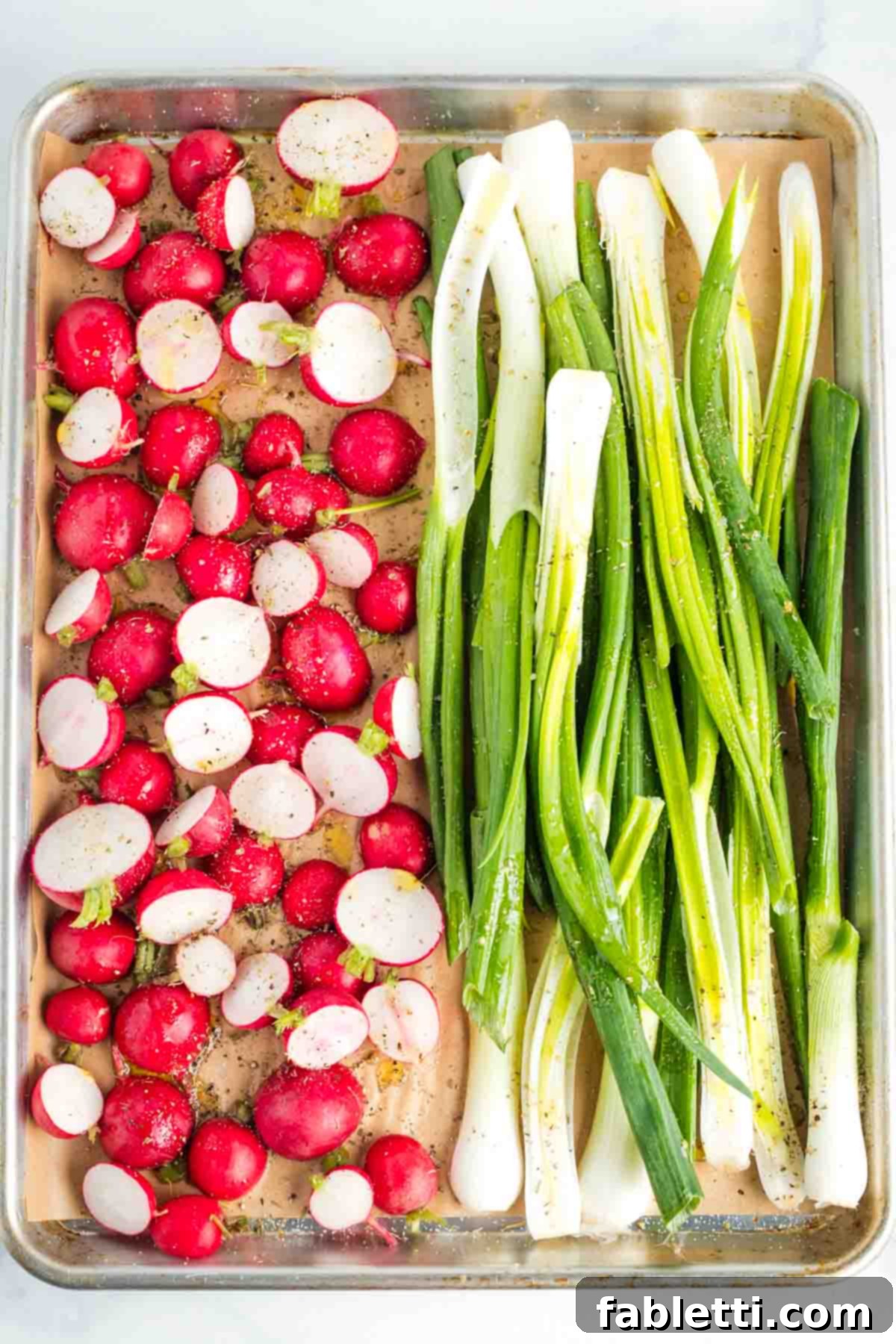 Roasted Radishes with Pistachio-Parsley Drizzle 6 Halved radishes and long green onions on a baking sheet lined with unbleached parchment.