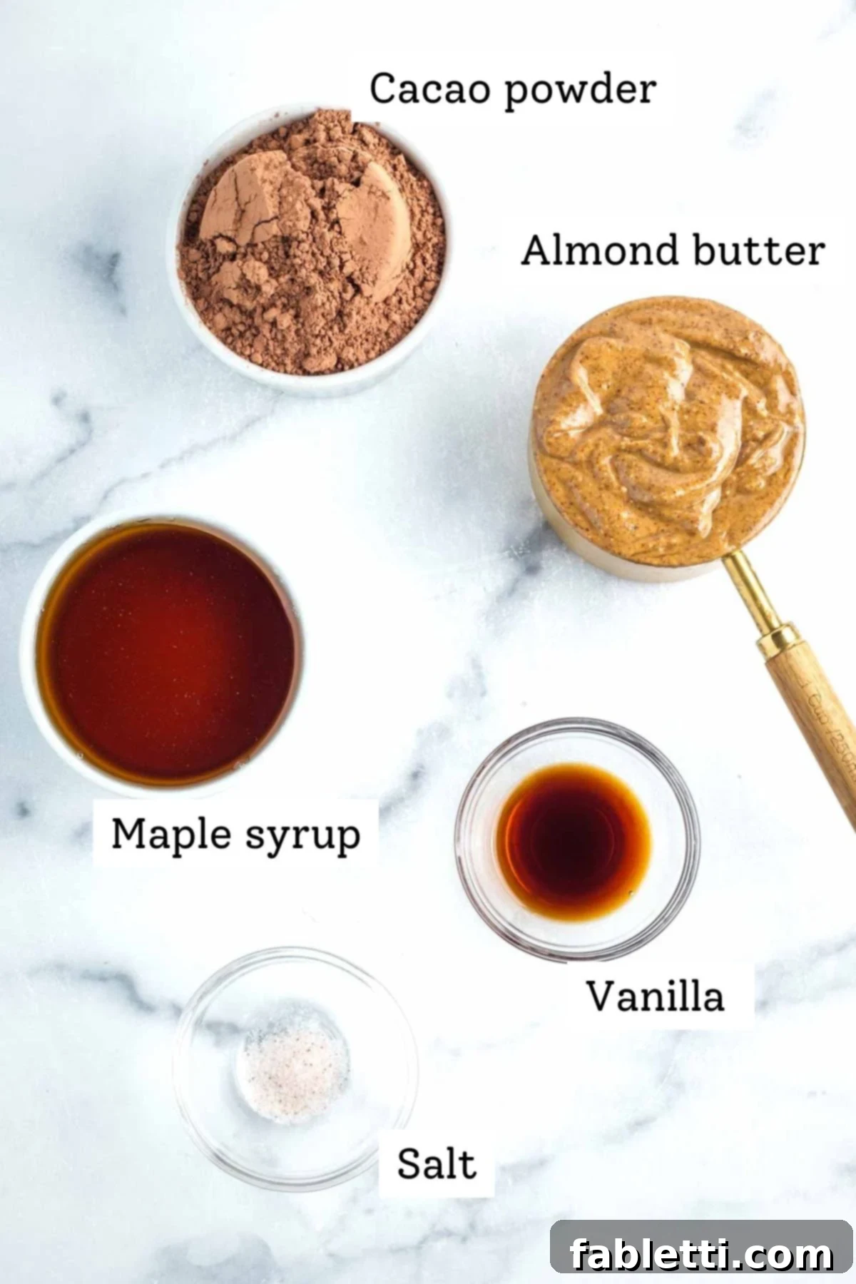 Beautifully arranged ingredients for vegan chocolate frosting: cacao powder, almond butter, maple syrup, vanilla extract, and a pinch of salt.