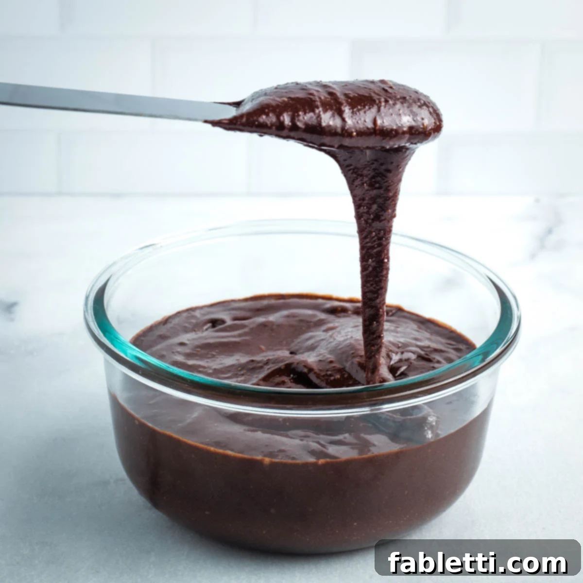 A pink spatula dripping with delectable chocolate frosting, showcasing its glossy sheen and smooth texture.