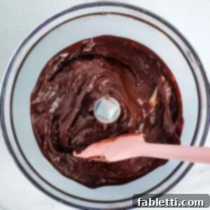 Close-up of a food processor mixing bowl with vibrant chocolate frosting.